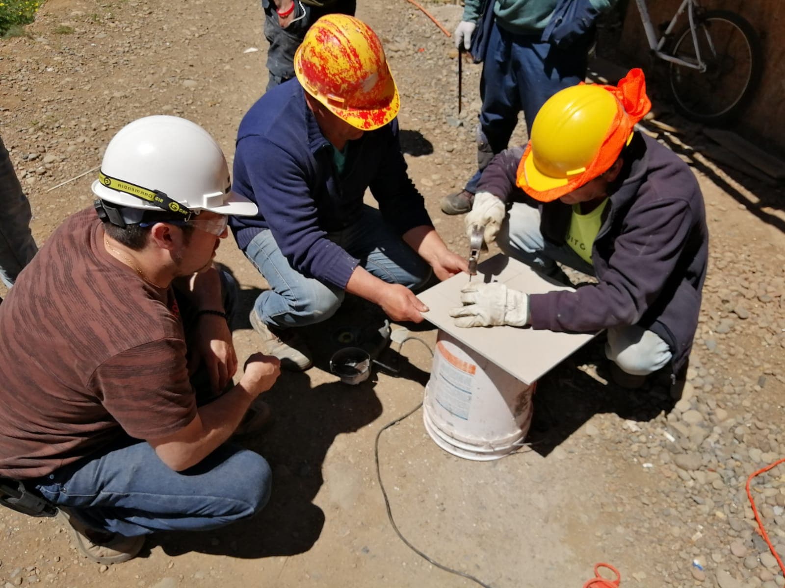 Trabajadores con casco practicando corte de cerámica durante una capacitación OTEC en plena obra